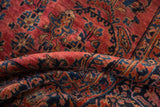 Folded vintage Sarouk carpet pile, showing plush texture and dusty raspberry red, navy floral motifs.