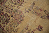 Antique Kermanshah carpet's muted camel field with faded cochineal florals and textural abrasions.