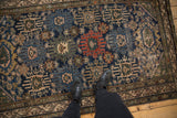 Vintage Malayer rug's repeating palmettes in navy blue, ivory, and madder red, with boots.