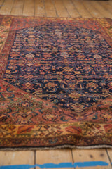 Deep blush floral main border, navy Herati field, and short fringe.