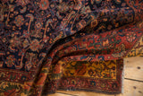 Unusual coloration across the folded Malayer rug, showing navy Herati motif, deep blush border, and gold palette.