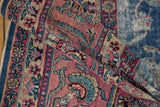 Worn vintage Yezd carpet detail showing raspberry field, blue vinery, and exposed foundation.