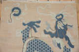 Distressed Tibetan rug shows dusty blue dragon scales and pale swirling motifs on a beige field.