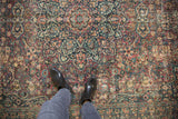 Distressed vintage Persian Meshed carpet with intricate scrolling floral patterns in wine red, navy, and sand tones.