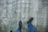 Distressed Kerman carpet with faded blue-green hues, worn pile, and visible foundation.