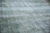 Worn texture of distressed Kerman carpet showing visible foundation and faded blue floral motifs.