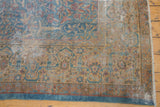 Distressed Persian Kerman rug corner with gold and blue dragon border and visible foundation wear.