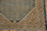 Distressed corner of a vintage Malayer rug, featuring denim blue field and sprawling spandrel plants.