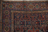 Close-up of antique Farahan Sarouk rug corner, showing Herati motif field and floral main border in madder root red and navy blue, with mostly even wear.