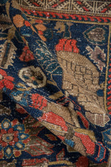 Rolled vintage Hamadan rug with navy blue, tomato red, and beige pomegranate leaf motifs.
