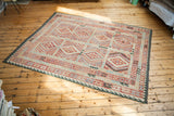 Angled view of the Kilim carpet's brilliant red, beige, and blue geometric patterns.