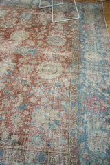 Angled view of a distressed Tabriz carpet with a worn red field against a wide sky blue border.