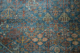 Distressed texture of a vintage Joshegan carpet, with intricate sapphire blue, ruby red floral motifs.