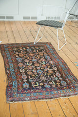 Kurdish rug corner: dark navy field, Herati and bird motifs, red and blue borders, worn fringe.