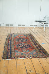 Antique Heriz runner with geometric medallions, brick red field, blue-green patterns, and textured pile.