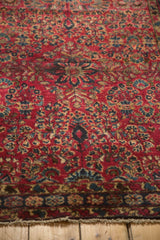 Vintage Lilihan rug corner, cherry red field, navy floral border, pale gold motifs, light fringe.