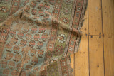 A draped antique Kurdish fragment shows the texture of its mir boteh pattern in slate blue, sage, and coffee brown tones.