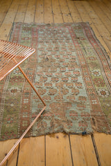 The soft, distressed wool pile of an antique Kurdish rug fragment with a repeating boteh design in sage and coffee tones.