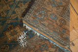 Visible repair stitching and frayed perimeter on antique Belouch rug in sapphire and copper.