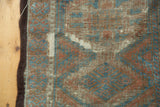 Distressed Belouch rug with thread bare rust and blue gul motif and tattered side.
