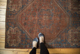 Feet on vintage Southwest Persian rug, showcasing a scalloped medallion in brick red and sapphire blue.
