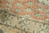 Distressed Turkmen rug pile with small hole, showcasing rust and beige geometric pattern.