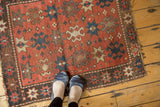 Hand-knotted antique Kazak rug with brick red field, navy blue crab, and beige starburst motifs.
