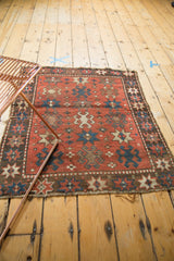 Antique Kazak rug corner detail, showing geometric starbursts, crab motifs, brick red field, and tattered fringe.