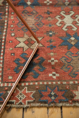 Antique Kazak rug's worn brick red pile with navy starbursts and geometric border details.