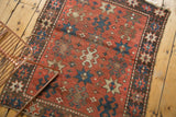 Brick red field of an antique Kazak rug with navy starburst and crab motifs.