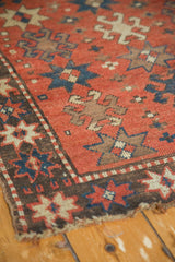 Antique Kazak rug corner, showing brick red field, dark border, and tattered end.