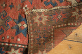 Antique Kazak rug's brick red pile with crab motif, tattered end, and woven foundation.