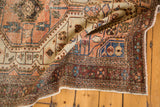 Distressed vintage Malayer rug corner showing worn pile, faded peach, blue, aubergine geometric patterns.