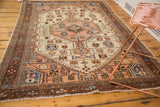 Corner of distressed Malayer rug with burgundy border, ivory field, peach vinery, and worn texture.