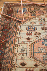 Close-up of distressed Malayer rug, showing geometric vinery in blush, ivory, and blue.