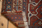 Antique Afshar rug corner showing fringe, madder red, navy blue geometric patterns, and pile wear.