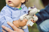 Close-up of baby's hands holding gray lion toy with brand tag visible.