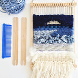 Tapestry weaving loom with textured blue, gray, white yarn and weaving tools.