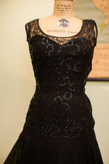 Vintage black lace evening gown with scattered sequins on a mannequin, highlighting drop-waist.
