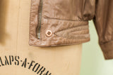 Light brown vintage leather jacket detail showing zipper, button, and pleated waistband.