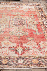 Angled view of distressed Oushak rug with faded red, silver, and charcoal patterns.