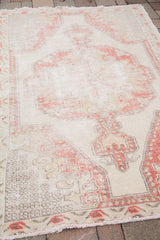 Distressed vintage Oushak rug showcasing faded red and ivory geometric motif.