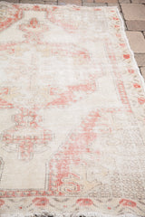 Distressed Oushak rug showing its soft texture, faded red and ivory motifs, and fringe.