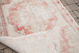 Distressed Oushak rug with faded red and ivory motifs, revealing its woven construction.