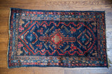 Indigo Lilihan rug corner, with bold red geometric patterns and time-softened fringe.