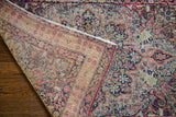 The turned corner of the antique Kerman rug reveals its distressed pile and fine woven foundation.