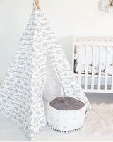 Open entrance of white teepee with gray arrows, round white pouf inside.